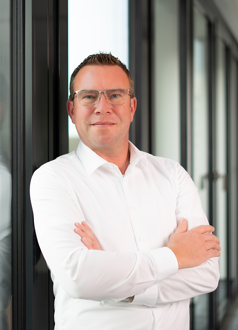 Evora team member, Dirk Rosenow, in a white business shirt standing confidently in a modern office environment.