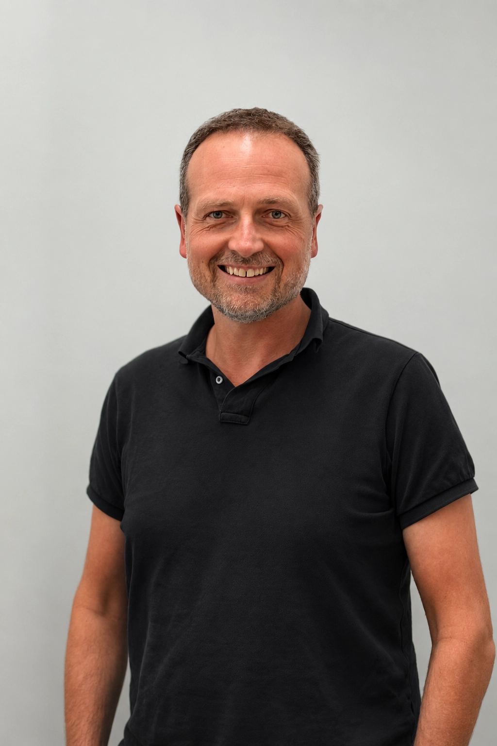Professional portrait of Marco Peters in a black polo shirt against a light studio background.